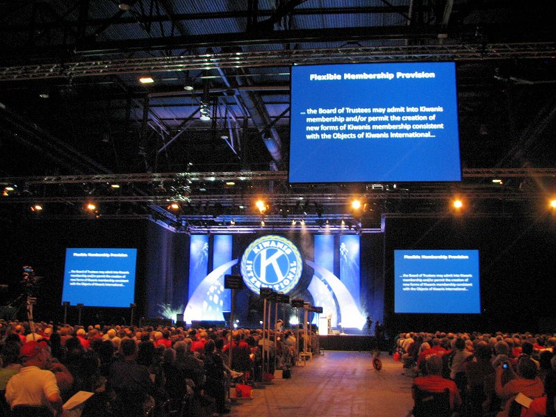 IMG_2924.jpg - Here is an attendee's overall view of the stage with the three jumbo screens so all can see the charts.  This explains the KI board encourages new and innovative creation of many new types of clubs 