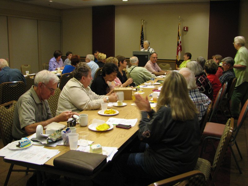 IMG_5395.JPG - In a long view, two roles of Kiwanians numbering thirty five plus attendees, are addressed by President Anna Lee Crockett.  Club Leaders from Bethesda, Potomac, Olney, Wheaton-Silver Spring, Montgomery Village, Mid-Montgomery, Rockville, and Leisure World provide 100% club attendance at the DCM.